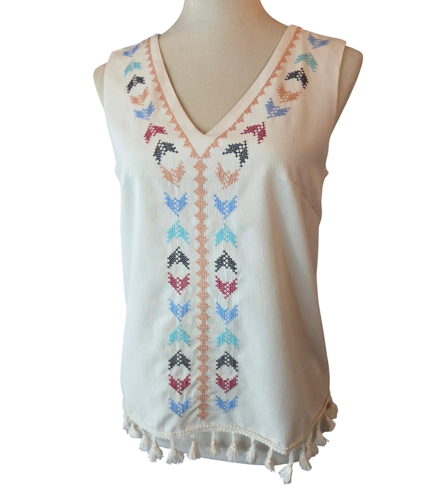 Birds of a Feather Boutique & Soy Wax Candle Company cream sleeveless V-neck blouse with colorful cross-stitch embroidery and tassel hem.